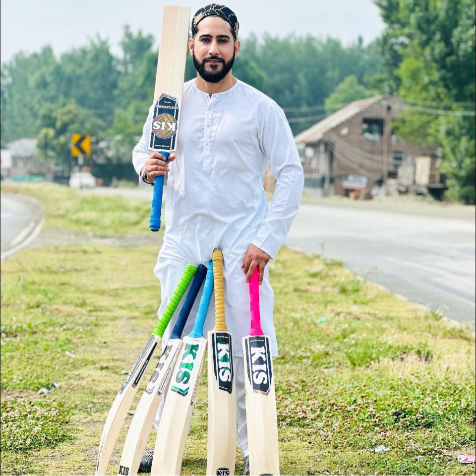 Man holding cricket bats and a bat with 'KIS Bats' branding outdoors. Best Kashmir Willow Cricket bats